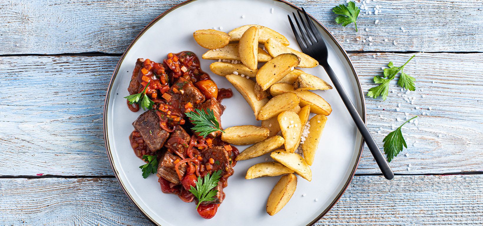Loomaliha guljašš tomatite ja peterselliga serveeritud koos Pati Parts Garlic kartulilõikutega